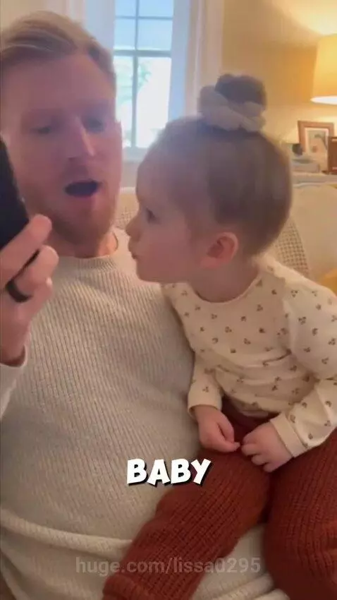 A man on a couch holds a young girl on his lap while on a phone call; the girl leans in to speak.