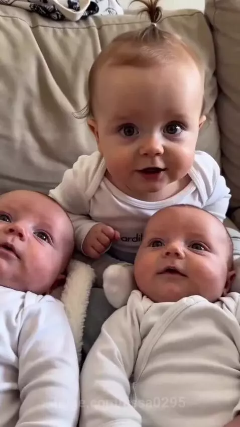 An older baby on a couch laughing uncontrollably after a fart sound is heard, with two younger babies nearby.