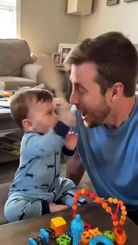 Baby boy in blue onesie holding a toy spatula, looking seriously at the camera.