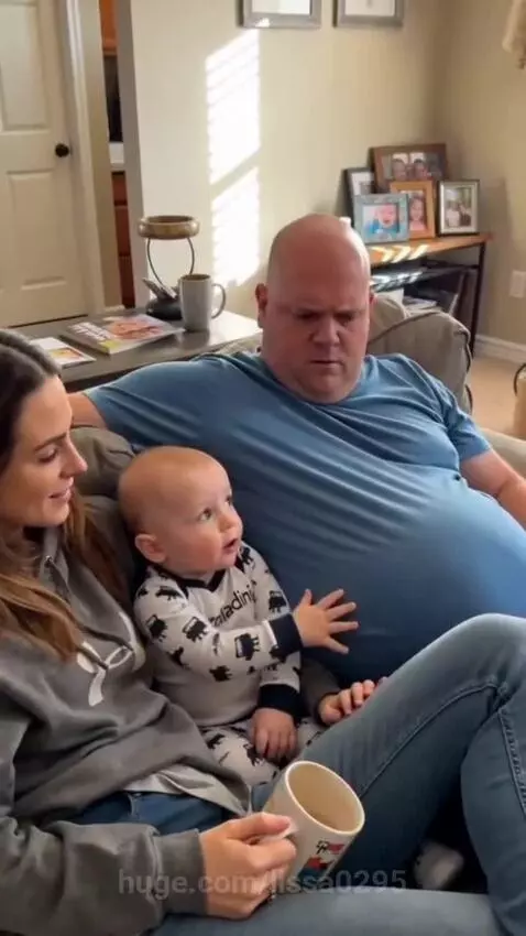 Baby points at dad's belly, thinking he's pregnant, while mom laughs.