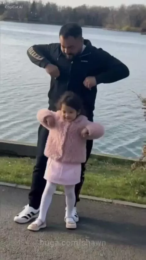 Father and young daughter dancing joyfully by a lake, both smiling.