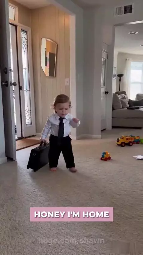 Toddler in a tie drops a briefcase and grabs a TV remote, heading for the couch.