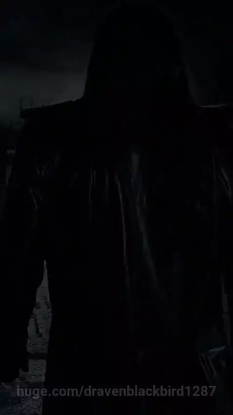 Person in a black trench coat walking through a dark, rainy graveyard with lightning.