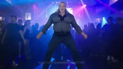 Man with grey hair and goatee dancing energetically in a club with purple and blue laser lights.