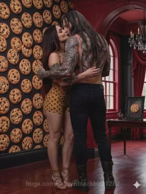 Shirtless man with tattoos and a woman in a polka-dot dress embrace in front of a wall covered in chocolate chip cookies.
