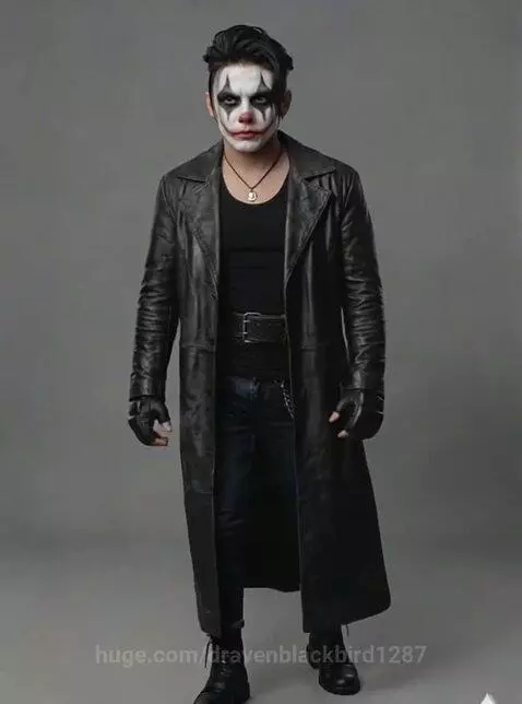 Man in a dark clown costume with white face paint and a black trench coat posing in a studio.