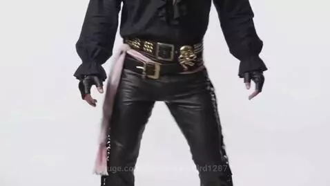 Person in black ruffled shirt, leather pants, and gloves shaking hips with a pink sash.