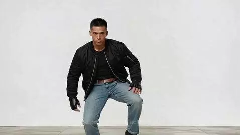 Man in black bomber jacket and fingerless gloves performing a martial arts side kick against a white background.
