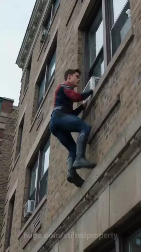 Man in red and blue superhero suit climbing up the side of a brick building towards an open window.