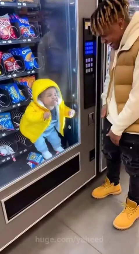 Man laughing at a vending machine with a baby-like figure trapped inside demanding Oreos.
