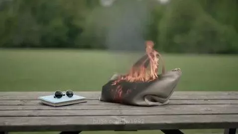 A light-colored purse on a wooden table ignites and is engulfed in smoke and flames.