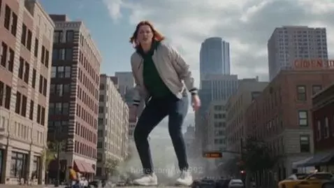 Giant red-haired woman in a green hoodie and jacket stands over a city street, looking angry.