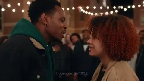 Couple engaged in a playful 'yo mama' joke battle outdoors at night, illuminated by string lights, with a smiling crowd watching.