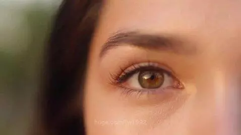 Extreme close-up of a female's hazel-brown eye with long dark eyelashes and a visible pupil.