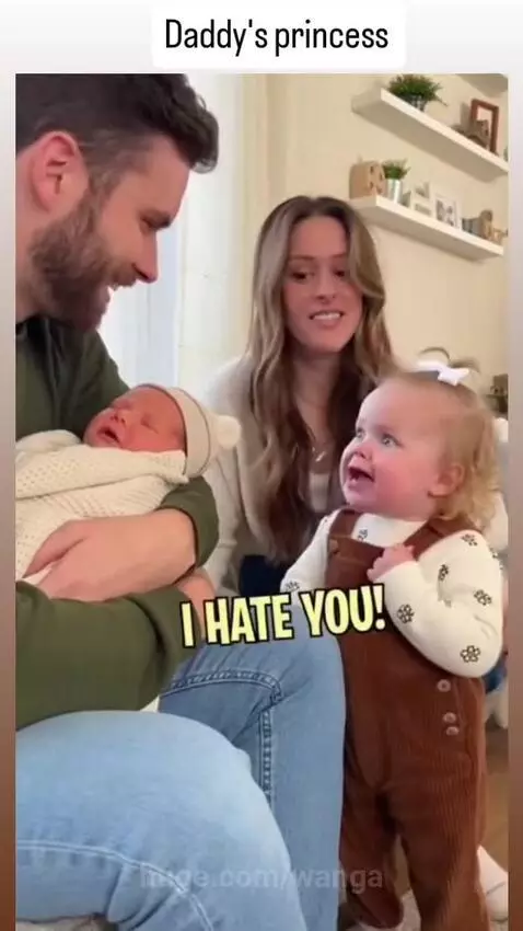 Toddler looking surprised and upset at a newborn baby held by their father.