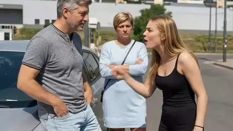 Young woman arguing assertively with an older man on a city street, with an older woman observing.
