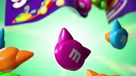 Vibrant cat-shaped candies resembling Skittles with a rainbow center, floating against a sparkling green background.