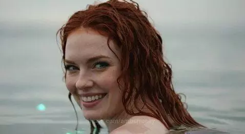 Woman with red hair partially submerged in water, man diving into the ocean, women watching on shore.