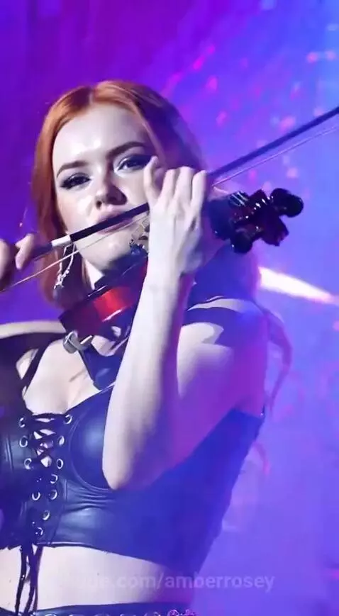 Amber Rosey performing a rock violin solo on stage with red electric violin, wearing a black corset.