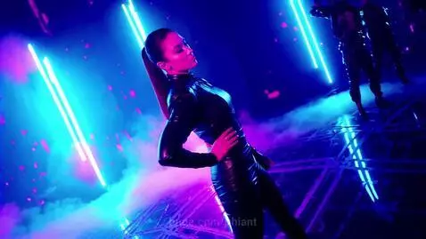 K-Pop idol in a black leather-like outfit with a high ponytail performs under blue and pink neon lights.