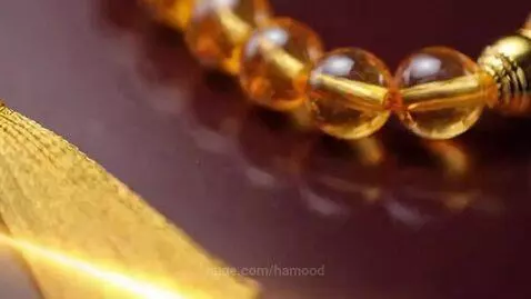Close-up of luxury tasbih prayer beads in blue, amber, and green with golden tassels against a dark maroon background.