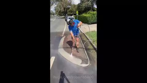 Man pressure washing a dirty brick and concrete median strip, revealing a clean surface.