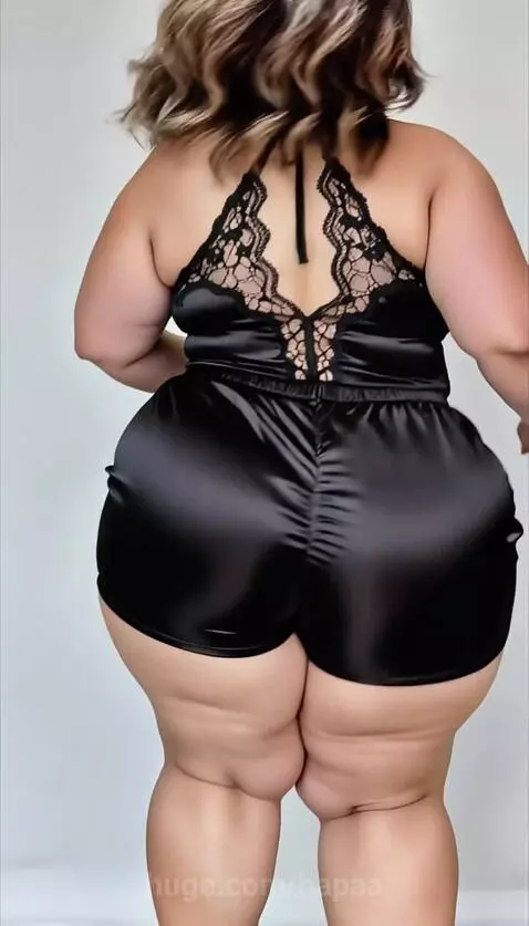 Plus-size woman wearing a black satin and lace romper and high heels, highlighting her figure.