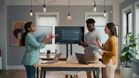 Three professionals collaborating around a table in a modern office with tech displays.