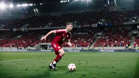 Football player in red and white uniform dribbling a soccer ball on a green field in a packed stadium.