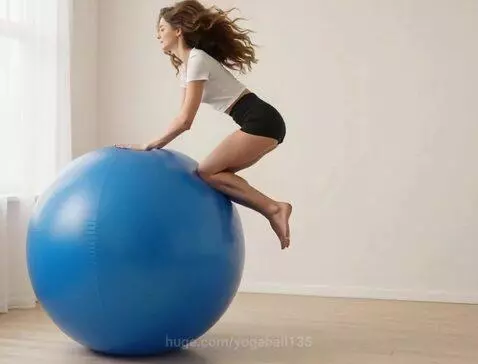 Young woman with long brown hair in a white crop top and black shorts jumping onto a blue exercise ball.