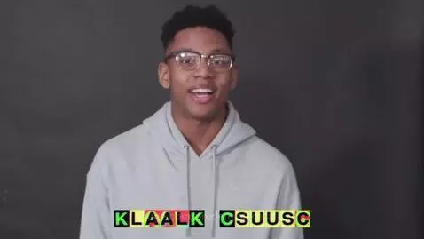 Man wearing glasses and a grey hoodie speaks to the camera against a dark grey background with colorful text overlay.