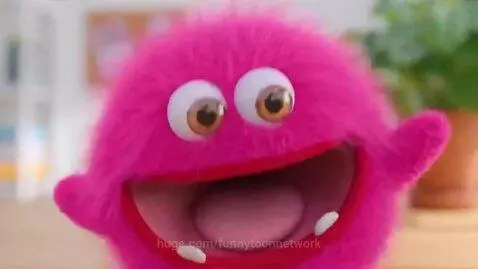 Fluffy pink monster with large eyes and fangs on a wooden surface, opening its mouth wide.