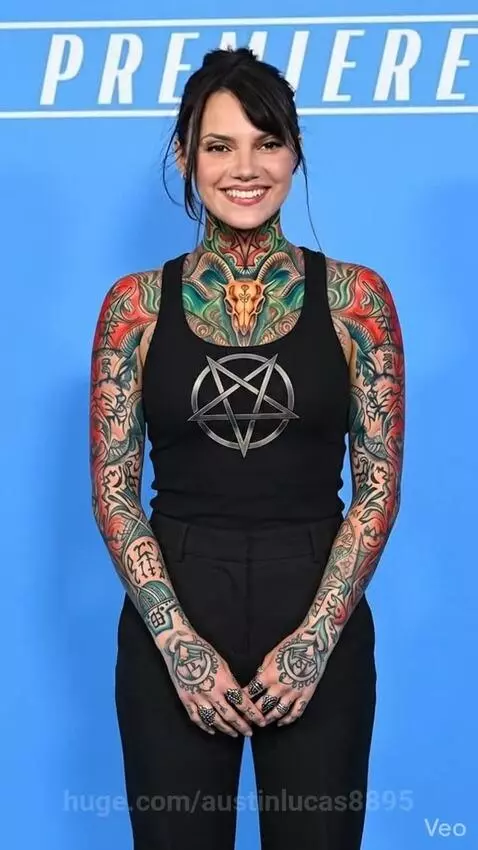 Woman with extensive colorful demonic-style tattoos on neck, arms, and hands, wearing a black tank top with a pentagram.