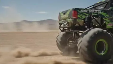Green, black, and white Monster Energy monster truck drifting in a dusty desert, kicking up sand.