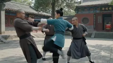 Woman in teal uniform performing martial arts, fending off six men in monk-like robes in a temple courtyard.