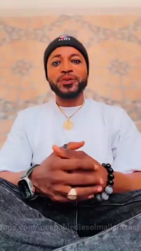 Man with beard, rings, and necklaces wearing a beanie, speaking directly to the camera.