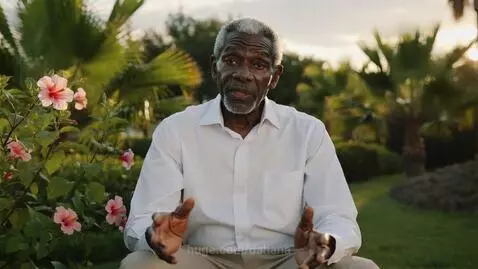 Elderly Black man with white beard in a tropical garden at sunset, sharing a message about discipline.