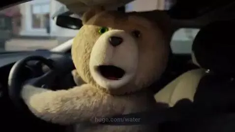 A scruffy teddy bear driving a car, looking at the camera, with a police officer in pursuit.
