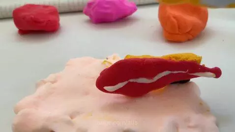 Close-up of hands manipulating colorful modeling clay on a white surface, creating abstract shapes.