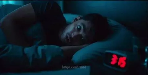 Man jolting awake in a dark room as an alarm clock blares loudly.